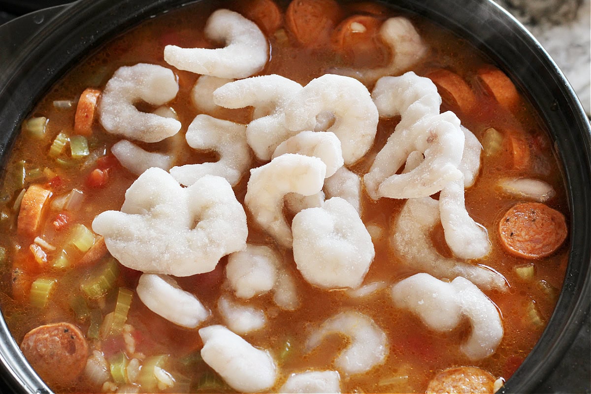 Frozen shrimp on top of gumbo jambalaya in a soup pot.