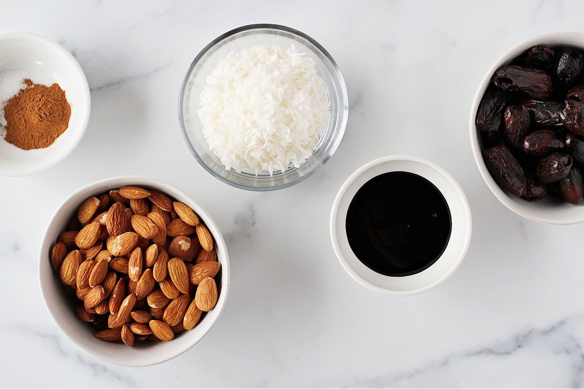 Raw almonds, shredded coconut, molasses, pumpkin pie spice and dates in bowls.