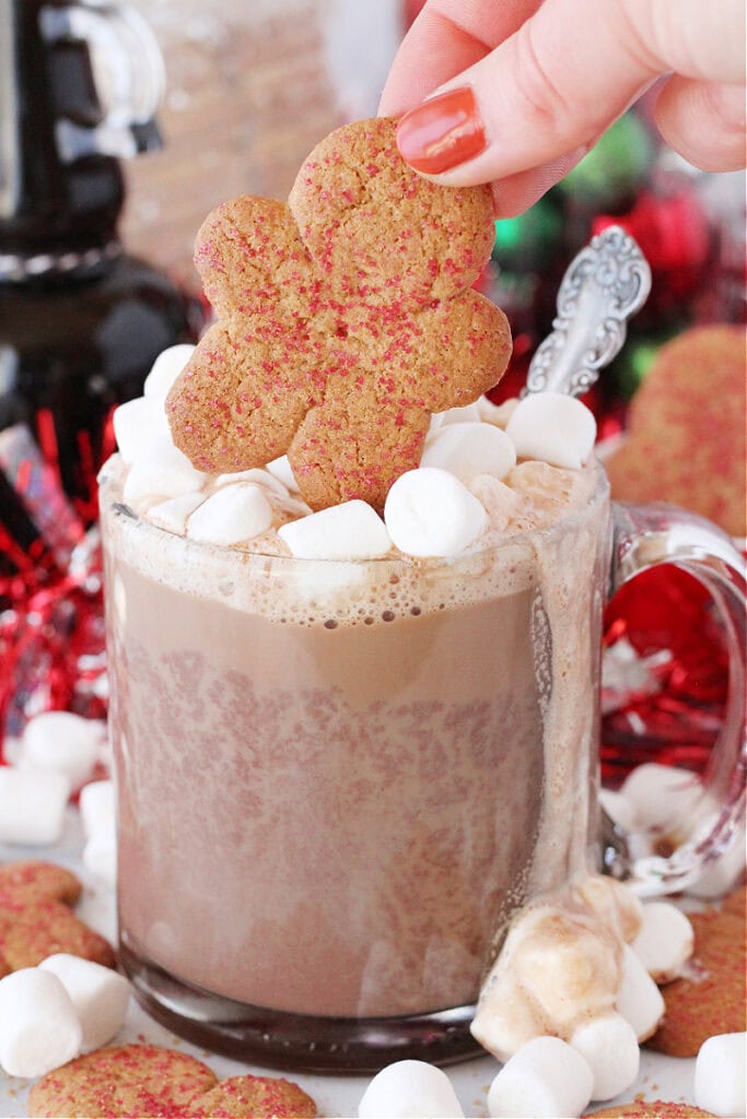 A woman's fingers placing a gingerbread man atop a mug of hot cocoa and marshmallows.