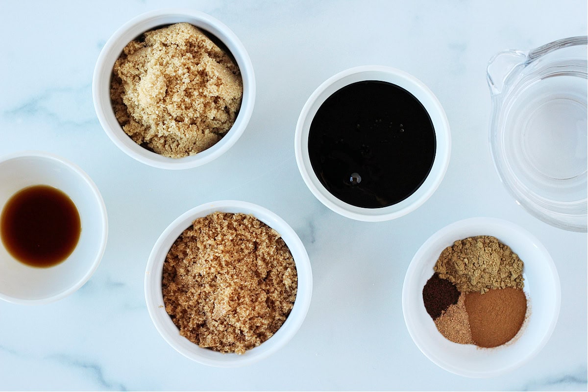 Bowls of ingredients for homemade gingerbread coffee syrup on a white countertop.