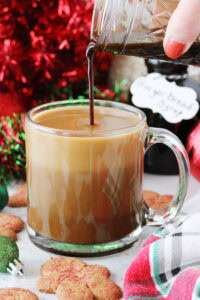 Pouring Gingerbread syrup into a mug of coffee surrounded by Christmas decor.