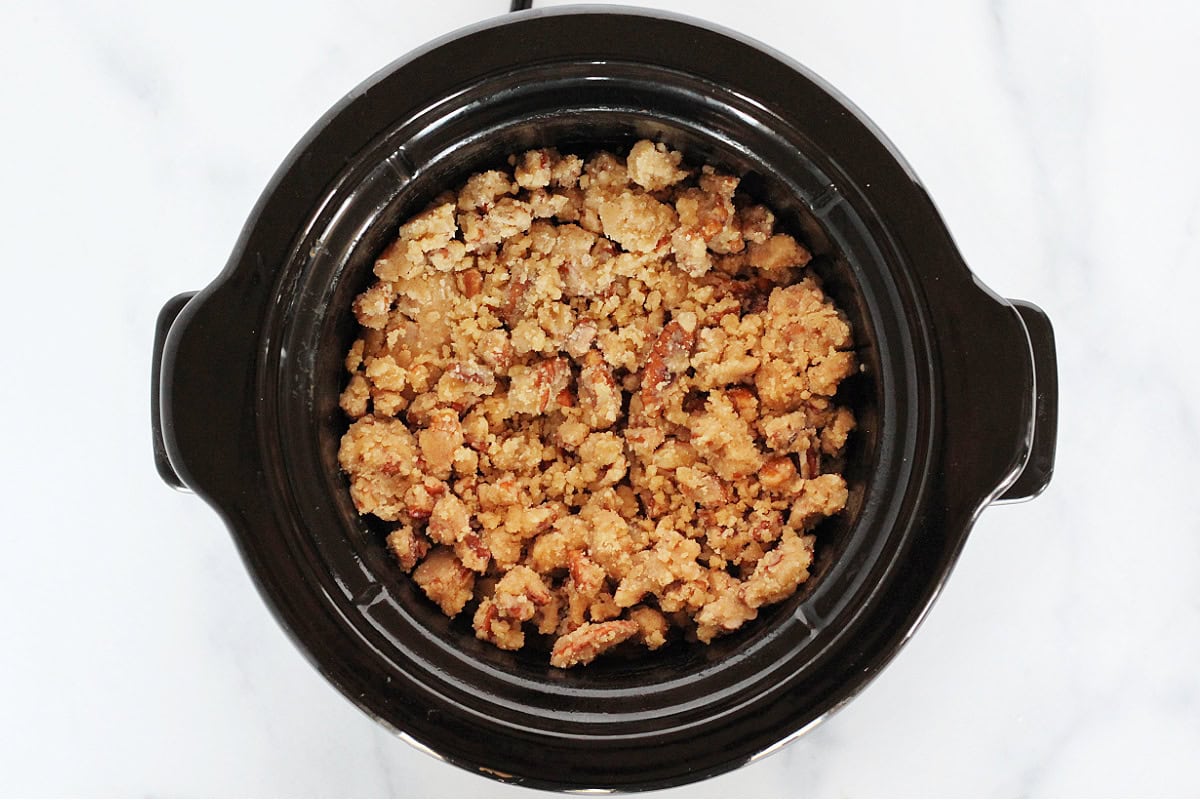 Overhead photo of raw pecan topping over sweet potatoes in a small slow cooker.