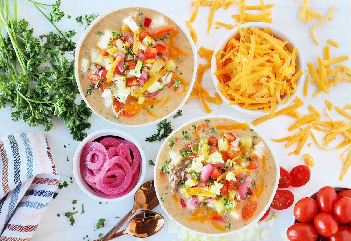 Overhead photo of easy cheeseburger soup surrounded by shredded cheese, veggies, and parsley.