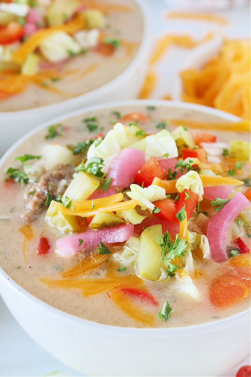 Up close photo of a white bowl filled with Cheeseburger Soup and toppings.