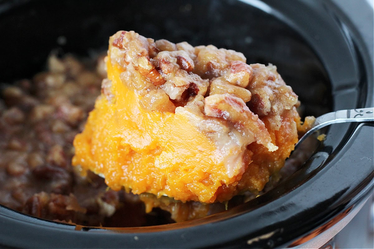 Up close photo of healthy sweet potato casserole on a spoon over the crockpot.