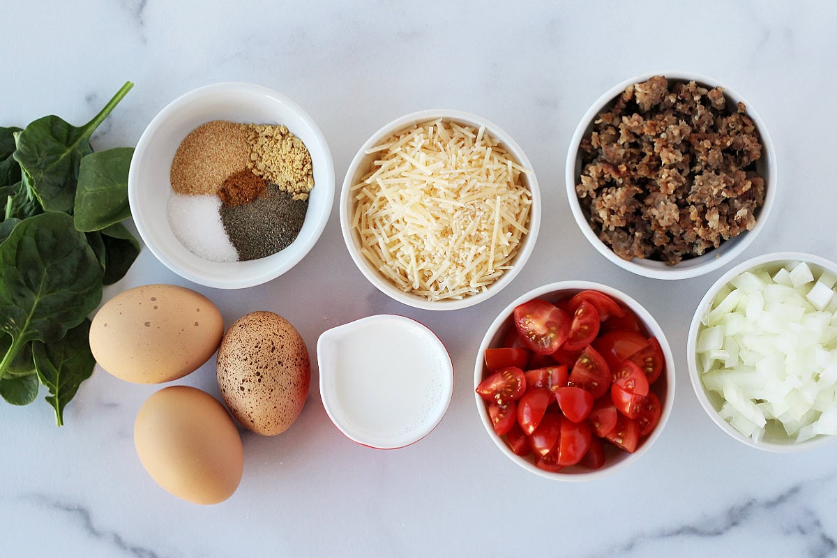 Ingredients in bowls for turkey sausage egg casserole with veggies on a marble countertop.