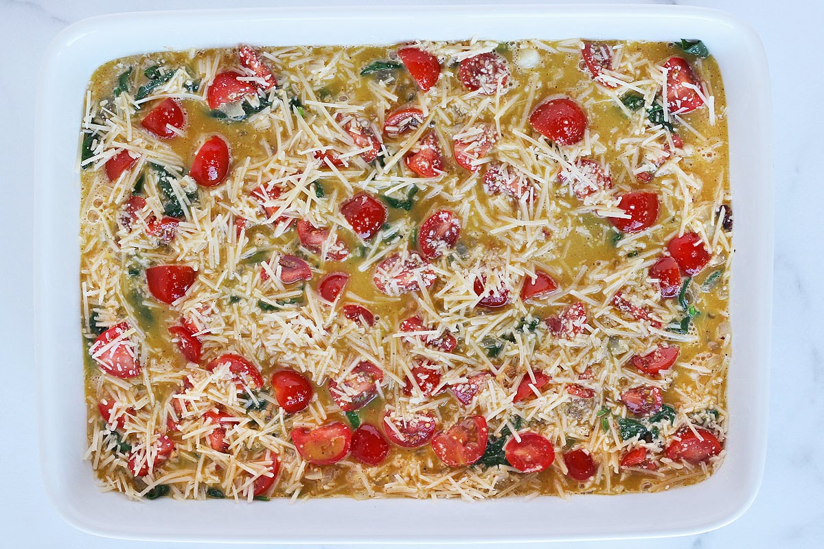 Overhead photo of an unbaked egg casserole with Parmesan cheese and cherry tomatoes.