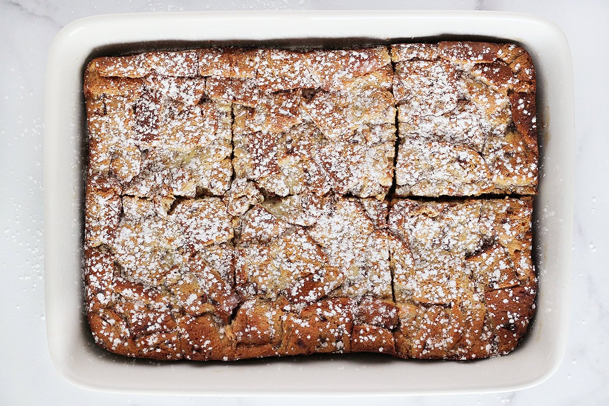 Baked caramel bread pudding topped with powdered sugar in a baking dish.