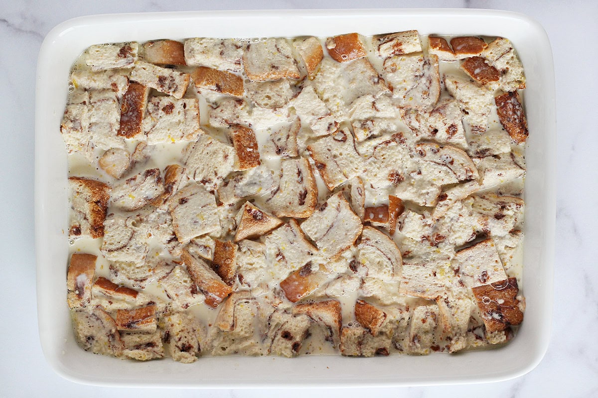 Cinnamon swirl bread pieces soaking in custard in a baking dish.