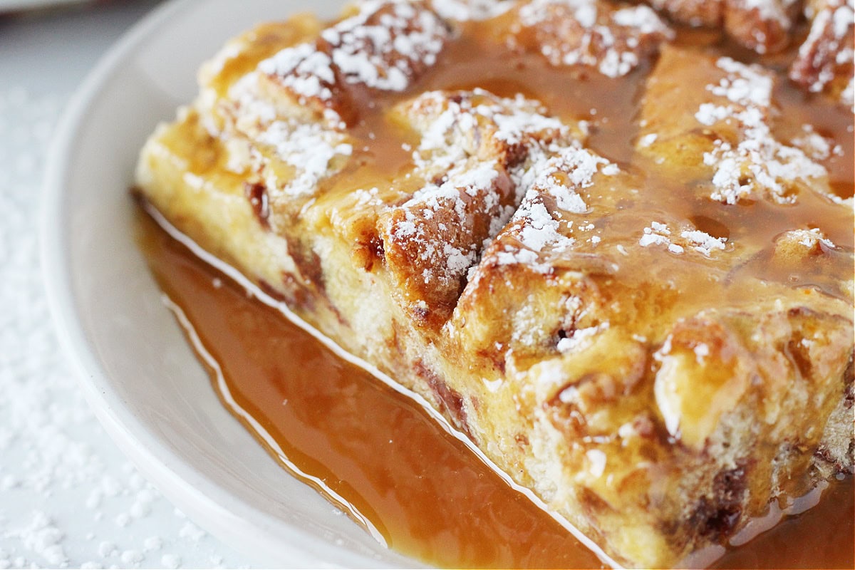 Close view of a slice of caramel bread pudding topped with powdered sugar.