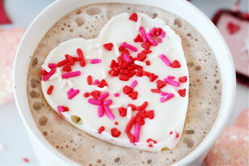 A pretty whipped cream frozen heart with sprinkles on top of hot cocoa.