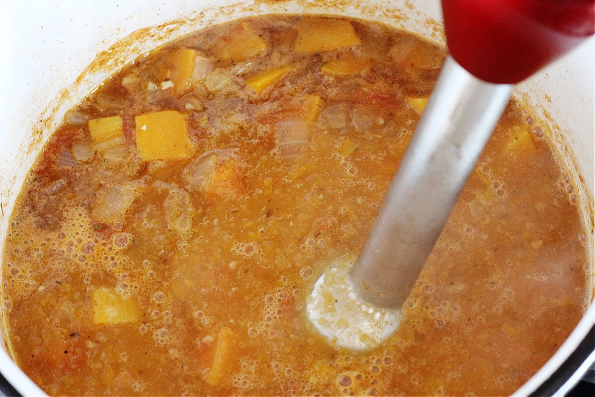 Immersion blender in a soup pot pureeing butternut squash soup.