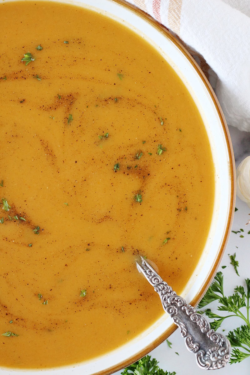 Pretty butternut squash soup in a bowl with swirls of parsley and black pepper.