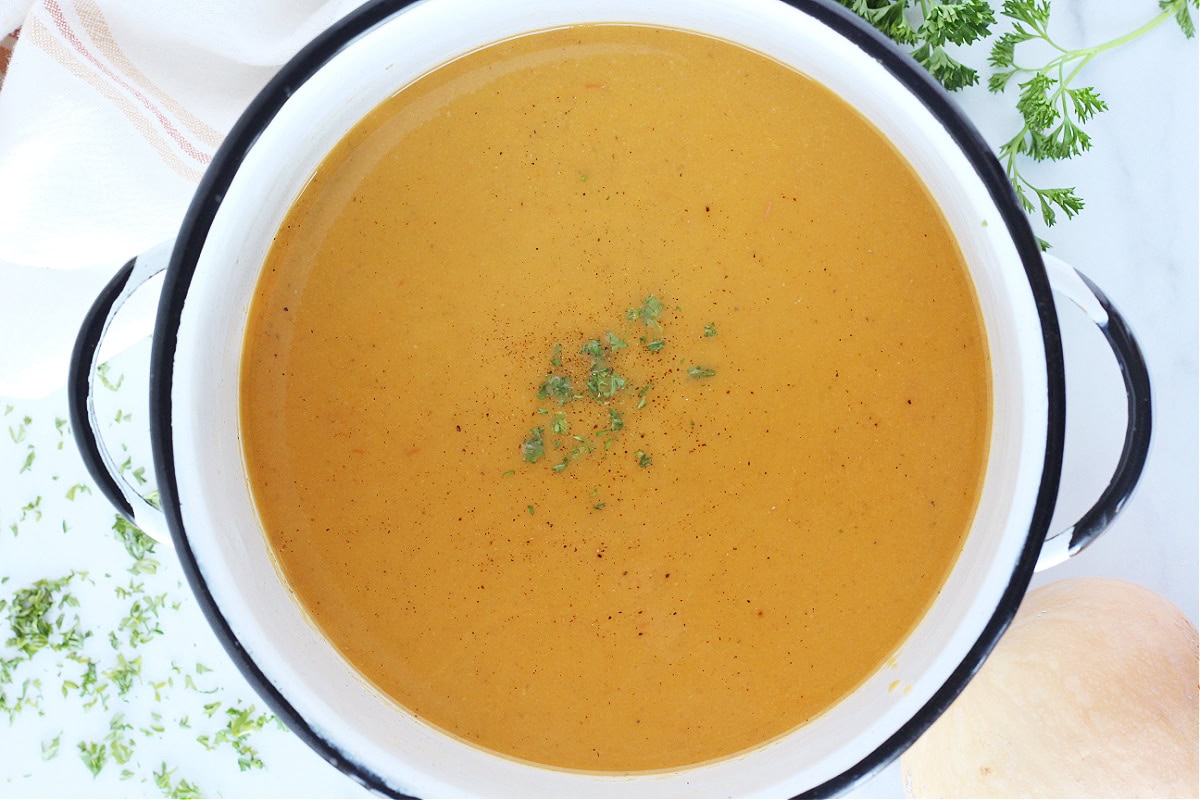 Overhead photo of a white pot with roasted butternut squash soup topped with parsley.