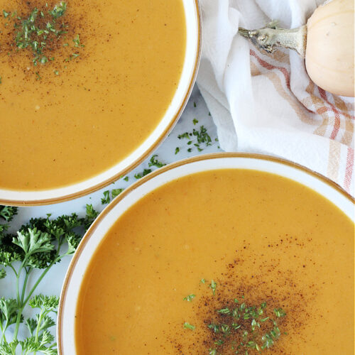 Overhead photo of two bowls of butternut squash soup topped with parsley and pepper.