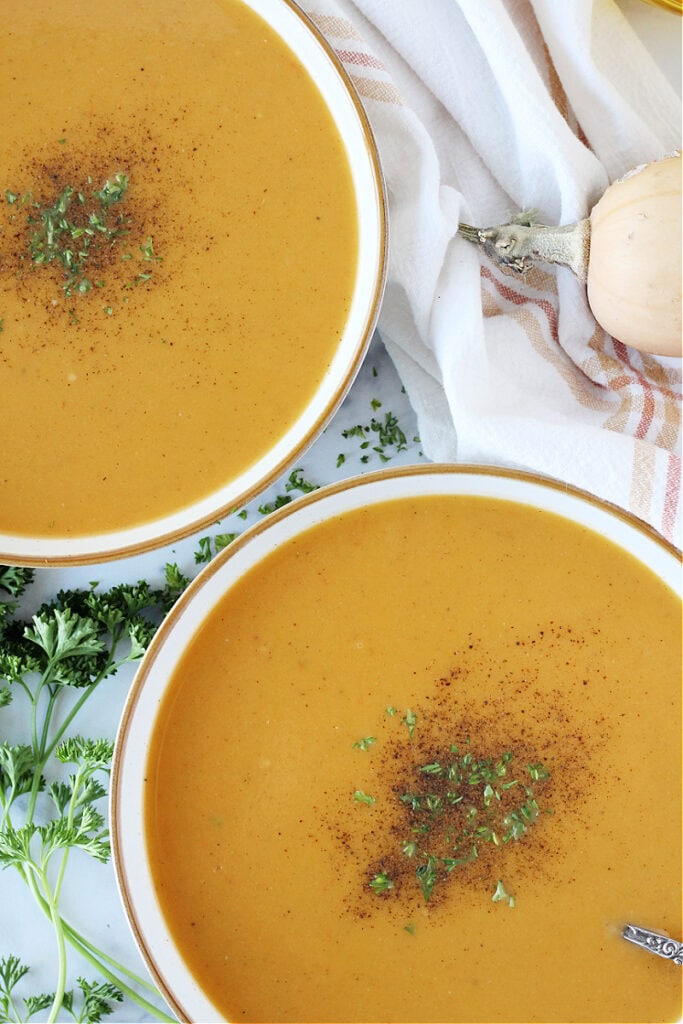 Overhead photo of two bowls of butternut squash soup topped with parsley and pepper.