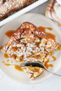 A slice of caramel bread pudding on a plate wtih a fork cutting a bite.