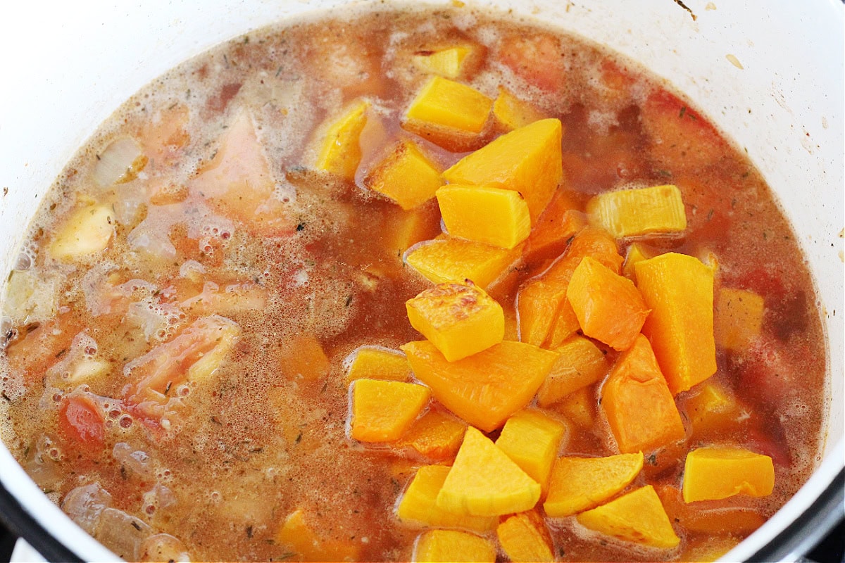 Roasted butternut squash cubes on top of vegetables and broth in a soup pot.
