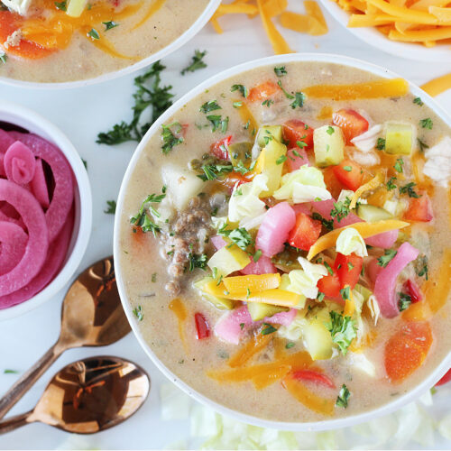 Overhead photo of a bowl of cheesy soup topped with pickled onions, pickles and cheese.