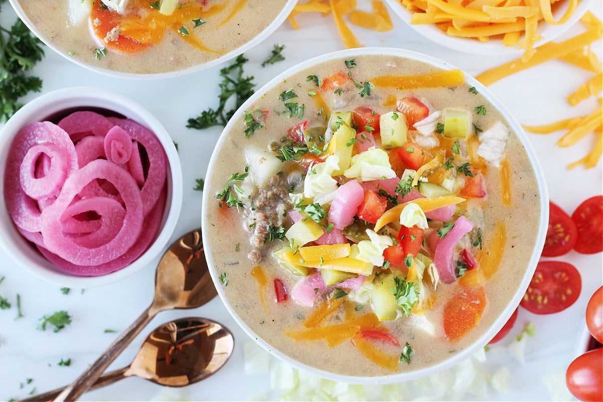 Overhead photo of a bowl of cheesy soup topped with pickled onions, pickles and cheese.