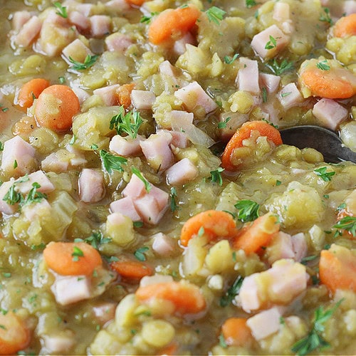 Split pea soup with diced ham in a bowl with a vintage spoon.