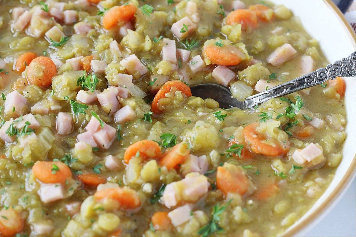 Split pea soup with diced ham in a bowl with a vintage spoon.