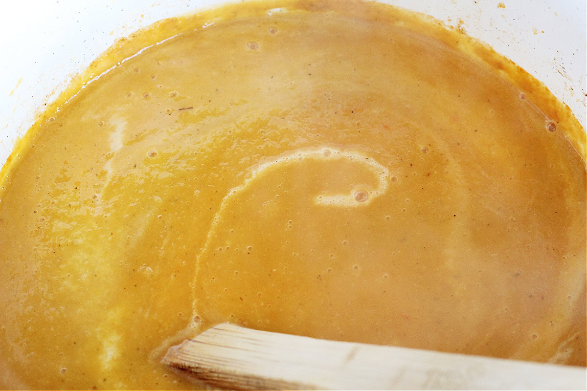 Wooden spoon stirring half and half into a pot of butternut squash soup.