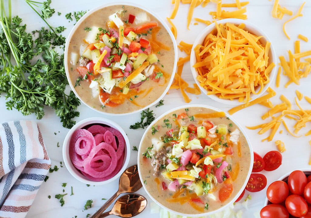 Overhead photo of easy cheeseburger soup surrounded by shredded cheese, veggies, and parsley.