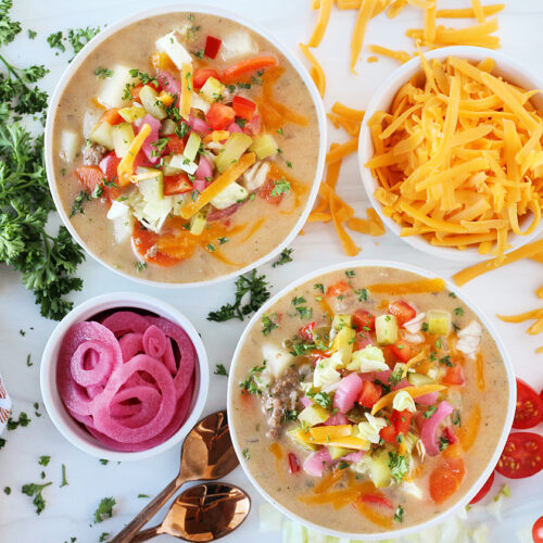Overhead photo of easy cheeseburger soup surrounded by shredded cheese, veggies, and parsley.