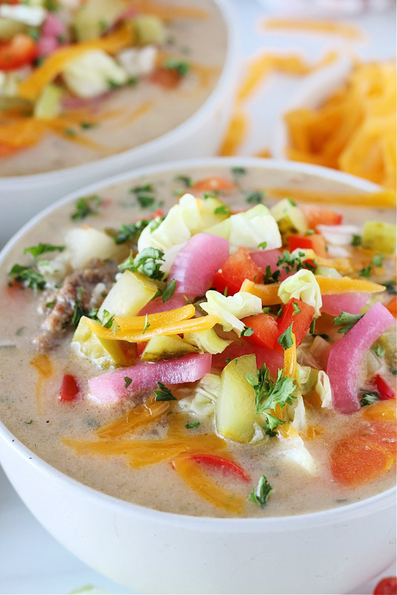 Up close photo of a white bowl filled with Cheeseburger Soup and toppings.