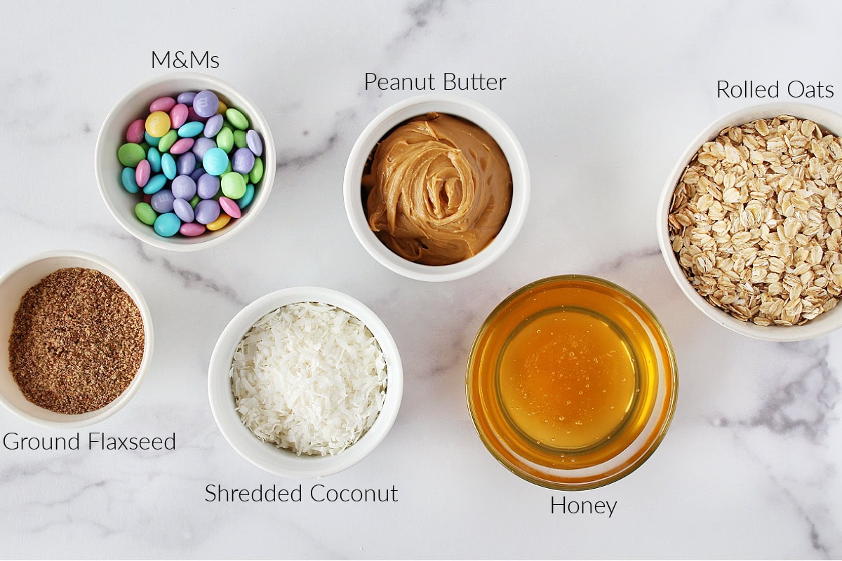 Labeled ingredients in bowls for no bake cookie bars with oats on a white countertop.