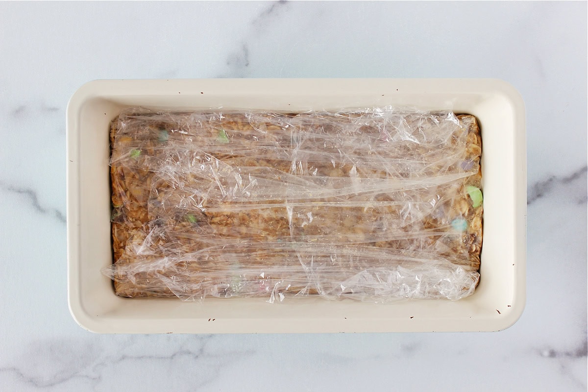 Cookie bars batter pressed into a bread pan lined with plastic wrap.