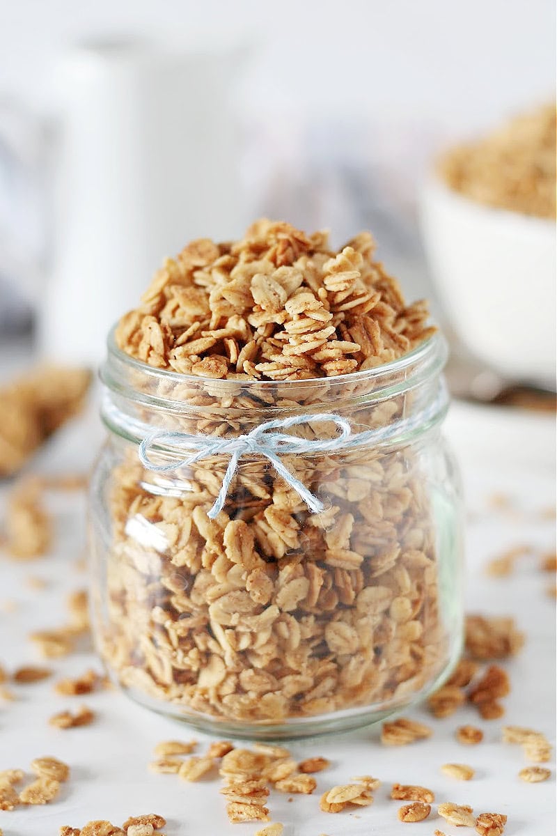 A clear mason jar with a blue string tied around it holding French toast granola.