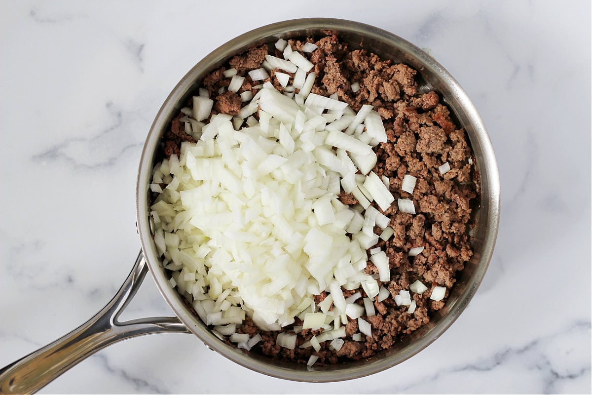 Diced onions on top of browned ground beef in a pan.