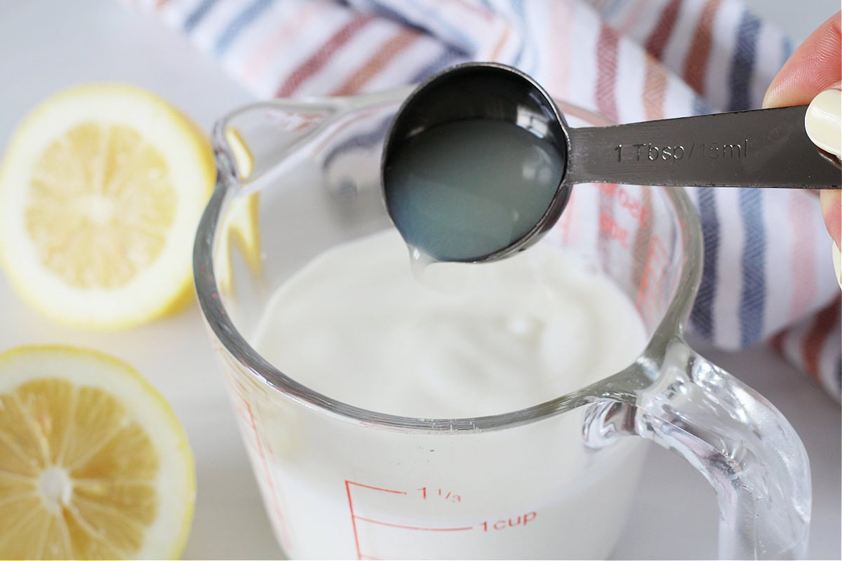 Pouring lemon juice into milk in a glass measuring cup.