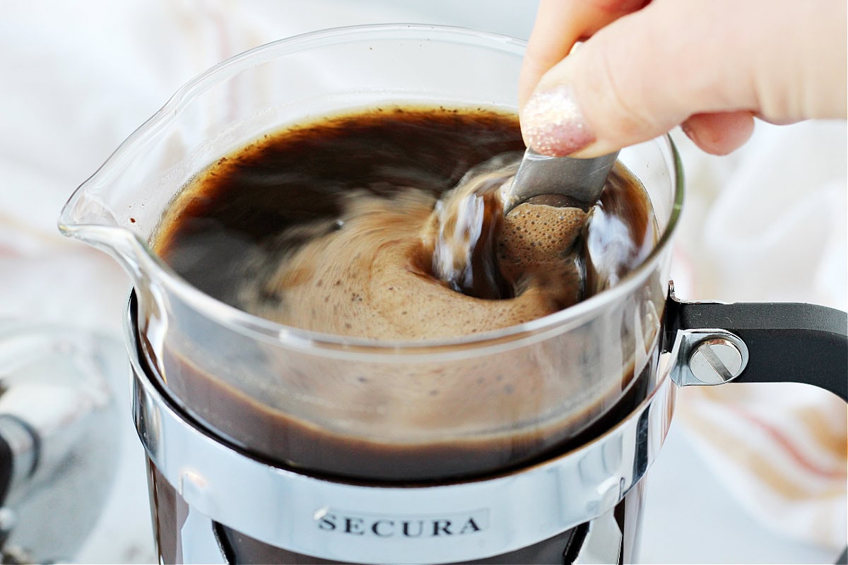 Stirring coffee grounds and water in a glass French press.
