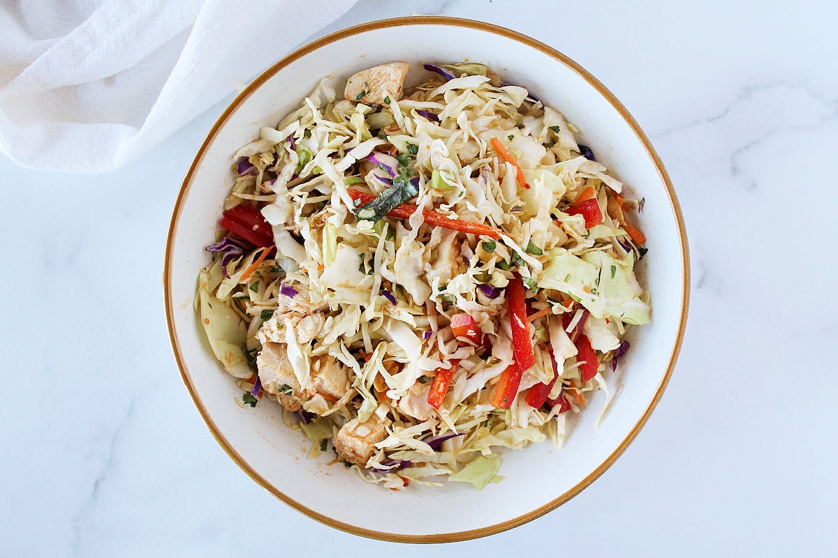 Coleslaw mixed with peanut dressing and chicken in a white bowl.