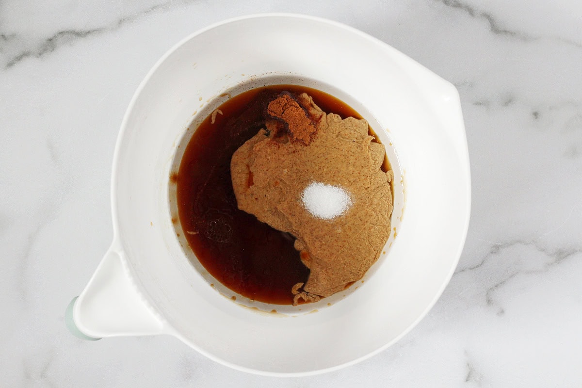Maple syrup, almond butter, salt, cinnamon and extracts in a white mixing bowl.