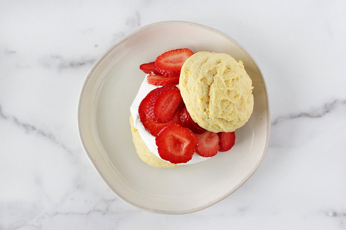 A lemon cookie topped with whipped cream, sliced strawberries and another cookie.