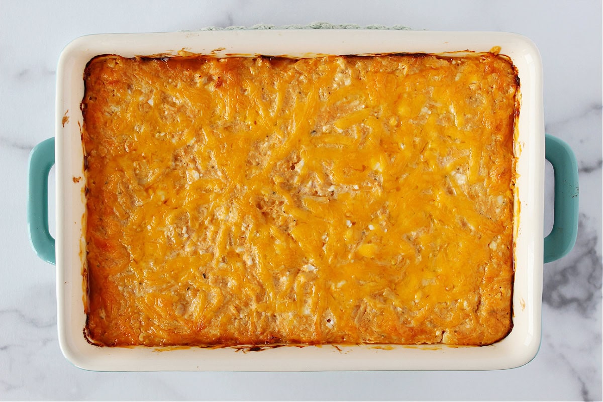 Baked buffalo chicken dip with melted cheese on top in a ceramic baking dish.