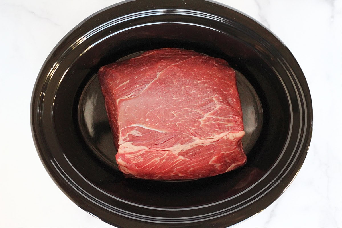 A large raw beef roast in a crock pot.