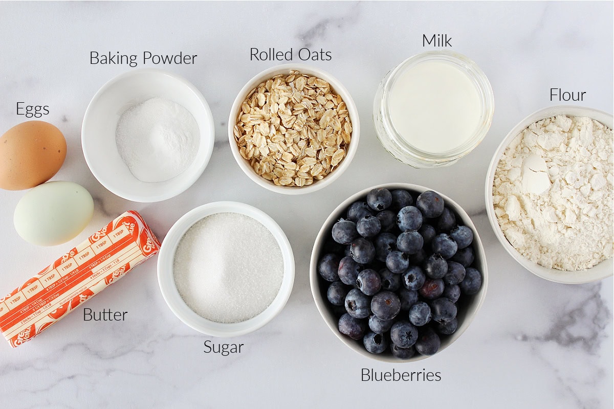 Labeled ingredients for blueberry coffee cake with crumble topping on a white marble countertop.