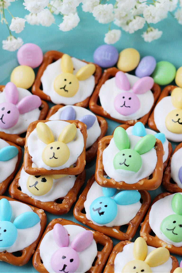 Easter bunny pretzels with pastel M&Ms on a light blue plate.