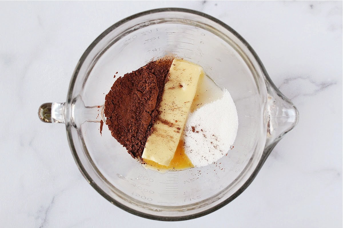 Cocoa powder, butter, sugar, and eggs in a glass mixing bowl.