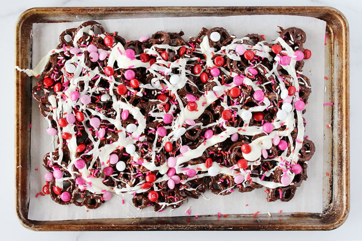 Red, pink, and white M&Ms and sprinkles topping chocolate pretzel bark.