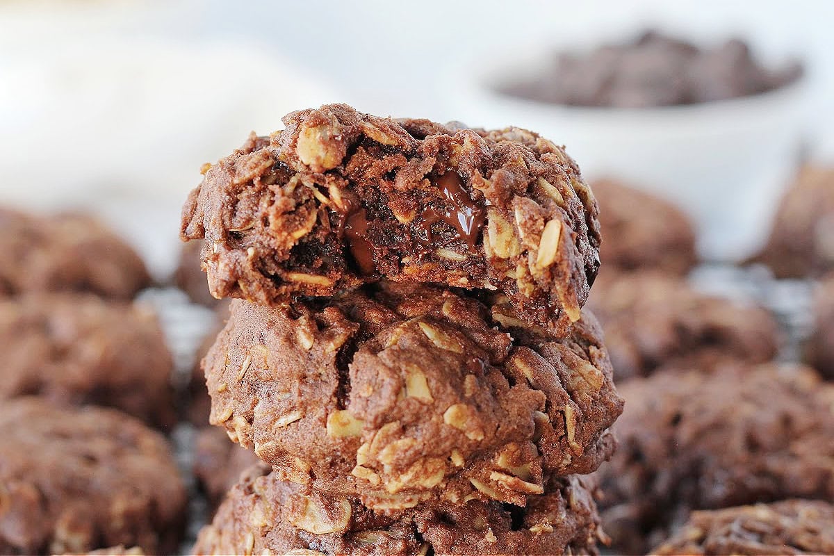 A bite taken out of the top cookie on a stack of chocolate oatmeal cookies.