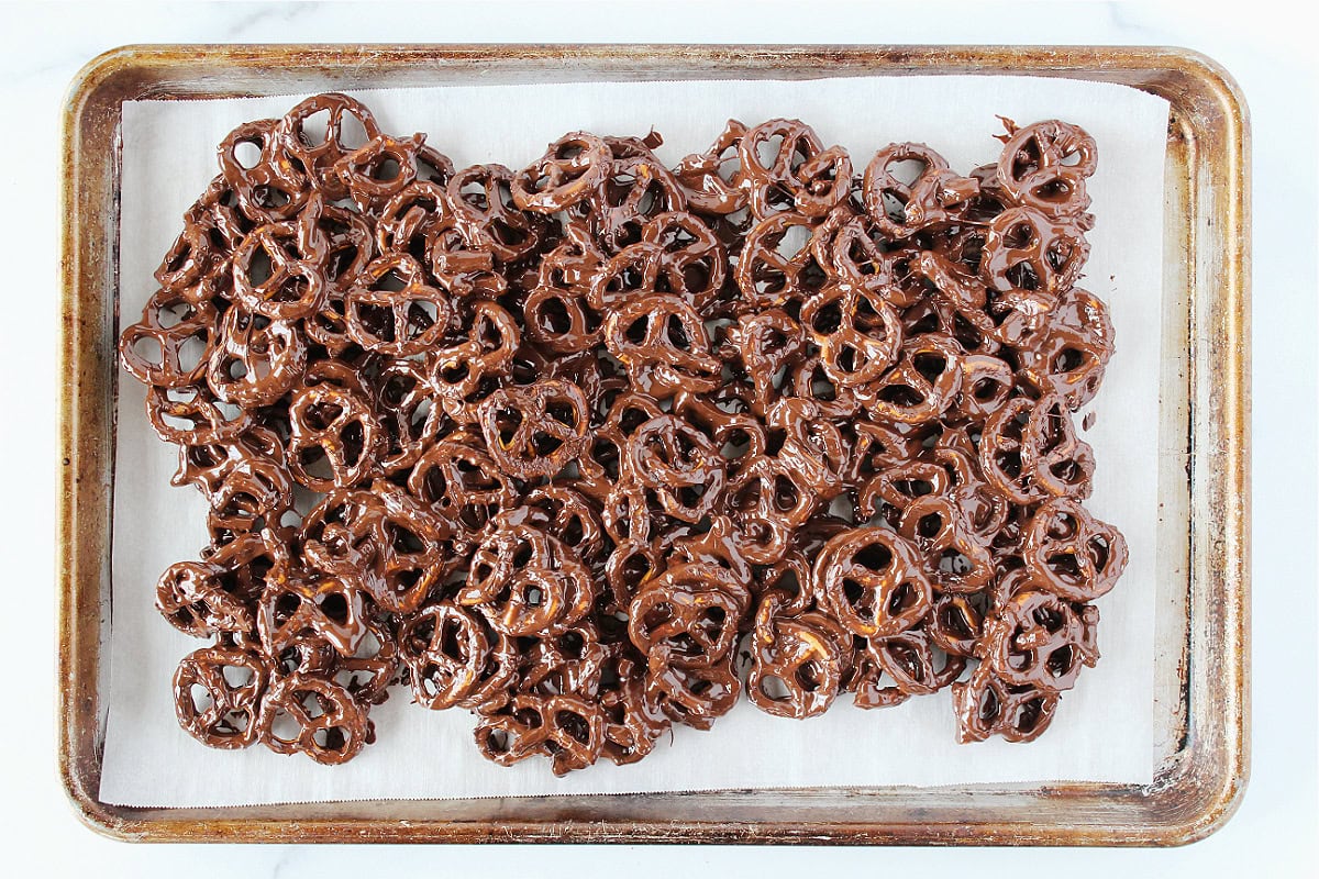 Twisty pretzels covered in dark chocolate spread out on a baking sheet.