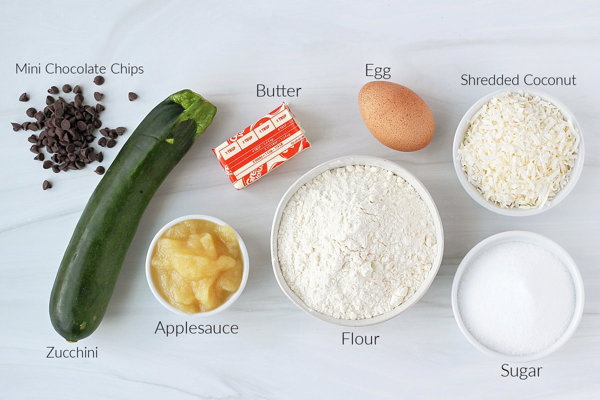 Labeled ingredients for zucchini chocolate chip cookies on a white marble countertop.