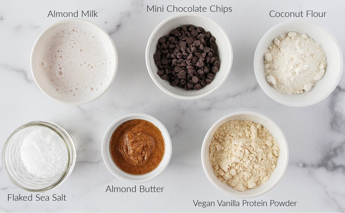 Labeled ingredients for high protein cookie dough bark on a white marble countertop.