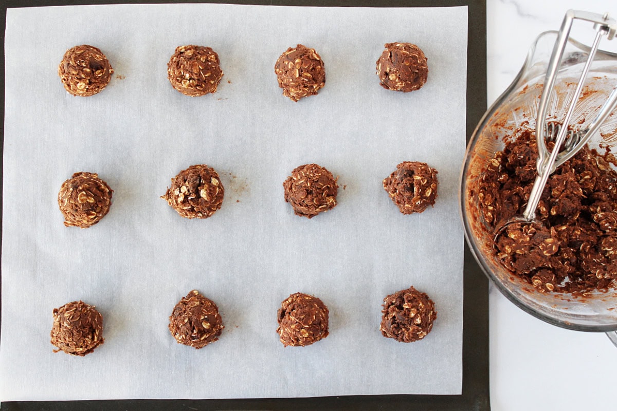 Twelve unbaked chocolate cookies on parchment paper on a baking sheet.